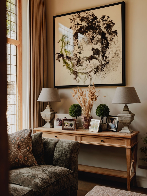 Elegantly styled hallway console table featuring abstract artwork, topiaries, and warm table lamps, ideal for home accessory marketing, Love Locations.
