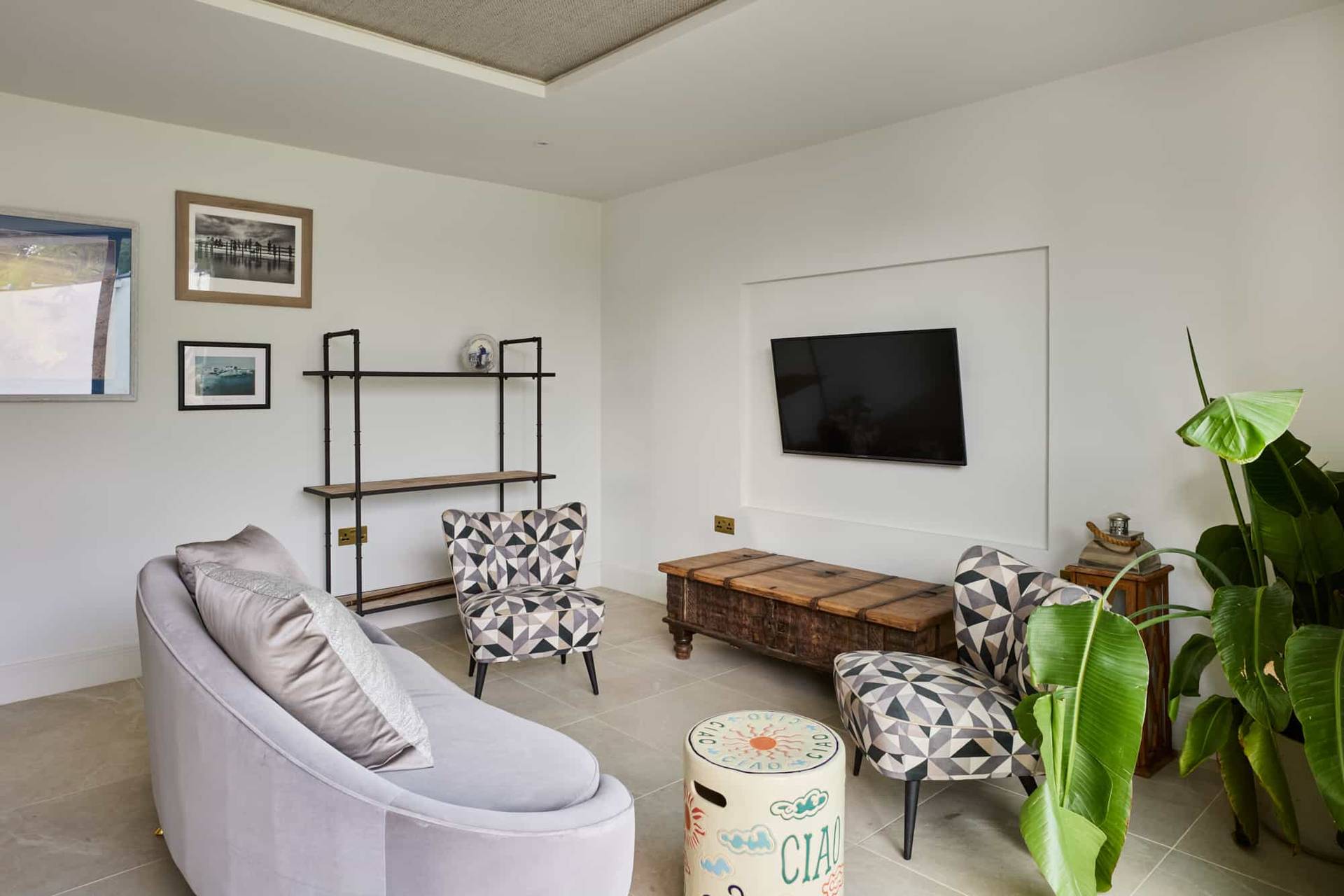 Secondary media room with built-in wall shelving, rustic coffee table, and patterned accent armchairs, Love Locations.