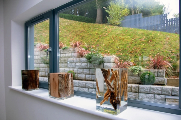 Artistic wooden decor accents arranged neatly on a wide windowsill framing a grassy hill exterior view, unique lifestyle backdrop by Love Locations.