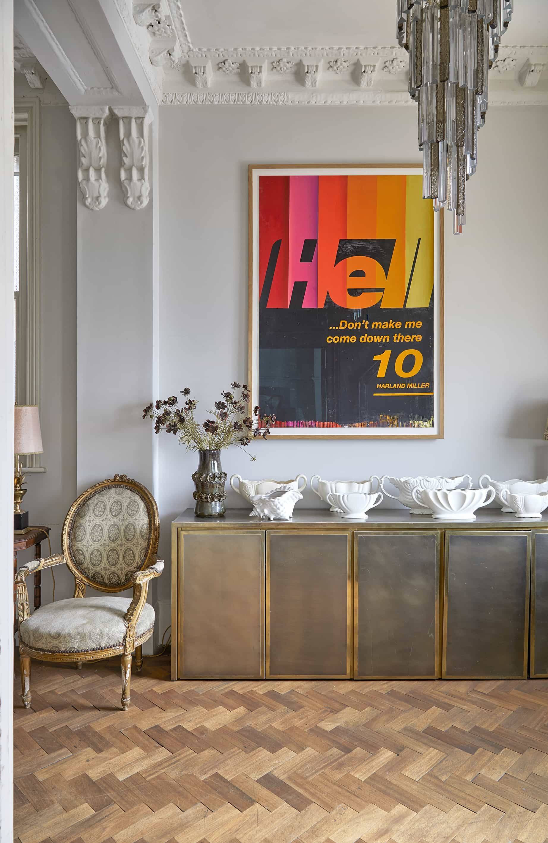 Brass sideboard console set against off-white walls styled with a yellow pop-art print and french armchair, Love Locations N16.