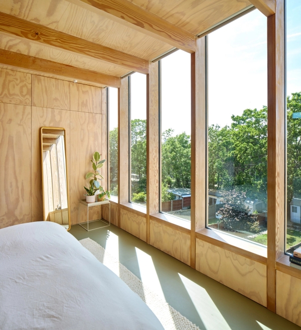 Sunlit master bedroom featuring plywood walls, concrete flooring, and garden view windows, Love Locations E17.