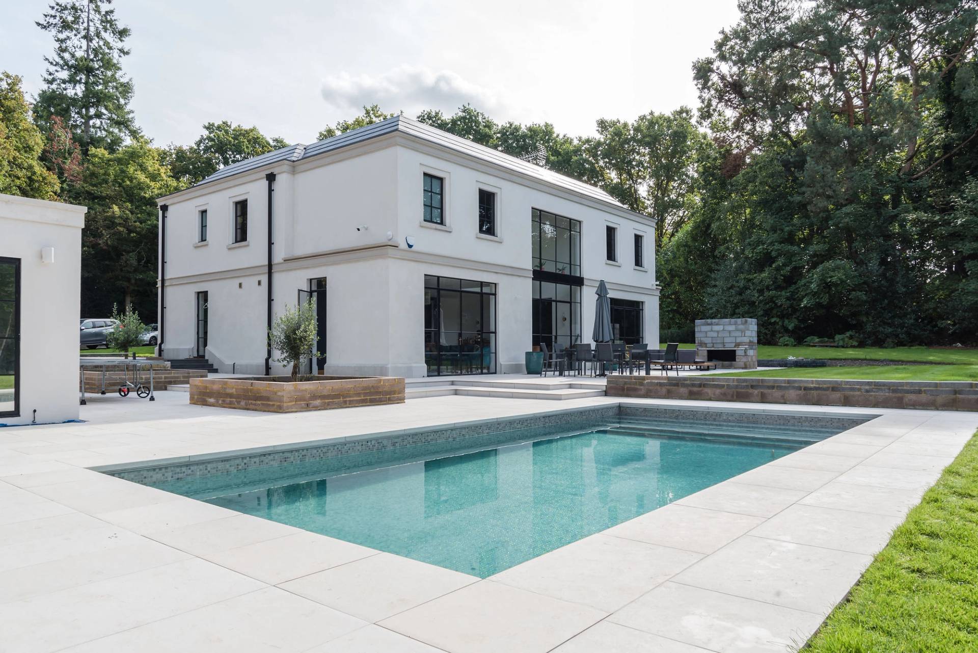 Luxury modern mansion back elevation featuring an outdoor heated swimming pool, paved sun terrace, and crittall doors, ideal for poolside shoots, Love Locations GU3.