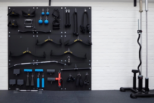 Wall-mounted functional fitness pegboard displaying specialized cable attachments, bars, and resistance accessories, perfect for fitness product photography, Love Locations SO23.