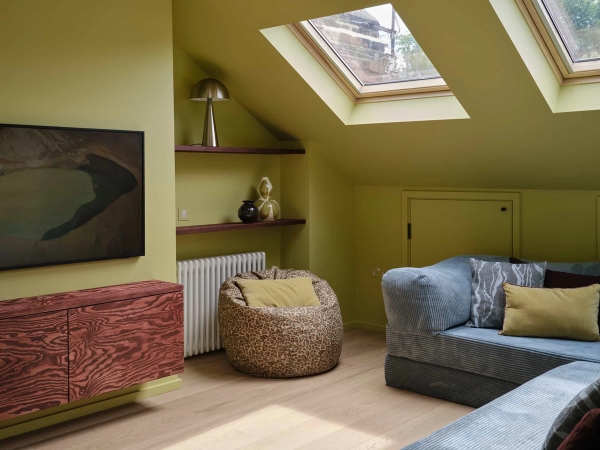 Love Locations character attic bedroom SE23: Cozy loft space with chartreuse walls, built-in wooden shelving, a skylight, and a grey sofa setup, tailored for relaxed lifestyle videos.