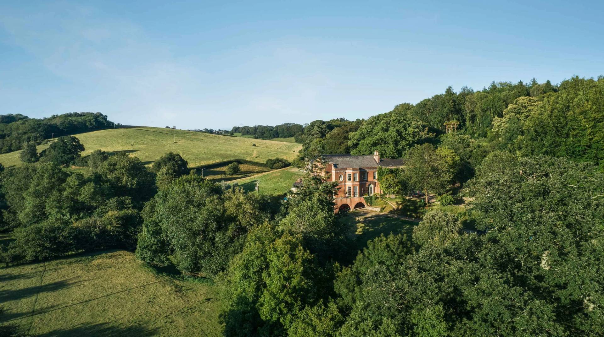 Wide countryside landscape showing a historic mansion house estate surrounded by rolling Devon hills by Love Locations.