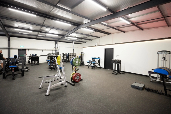 Open free-weight training zone featuring a loaded barbell and plate tree inside a spacious industrial-style gym location, Love Locations.
