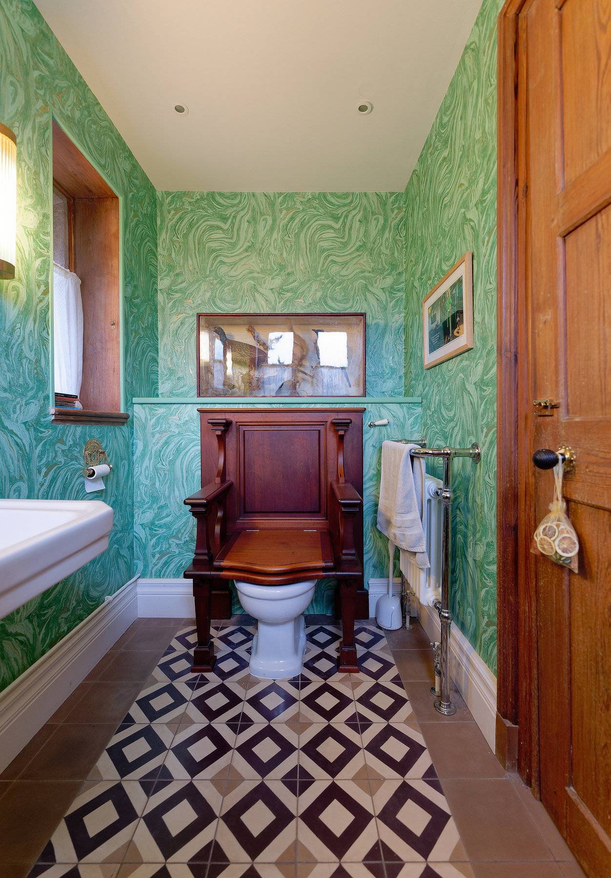 Green patterned wallpaper bathroom suite featuring a classic high-tank wooden toilet and tile floor, Love Locations OX7.