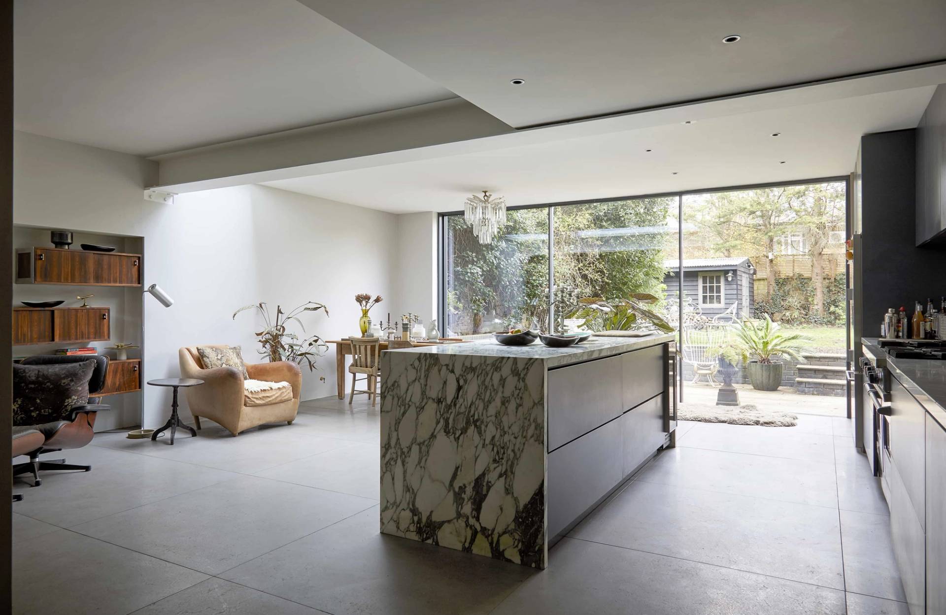 Dramatic dark veined marble kitchen island set on polished concrete flooring under soft recessed lights, Love Locations N16.