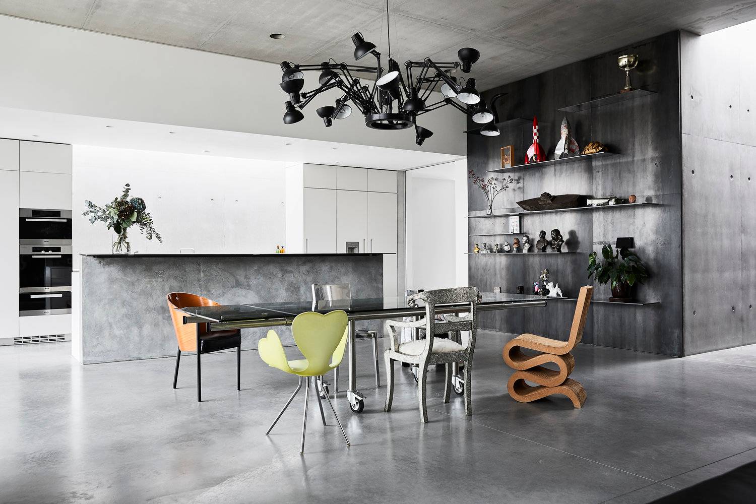 Open-plan architectural dining space featuring a long dark table, eclectic designer chairs, spider arm chandelier, and industrial concrete walls, ideal for luxury brand lookbooks, Love Locations SW8.