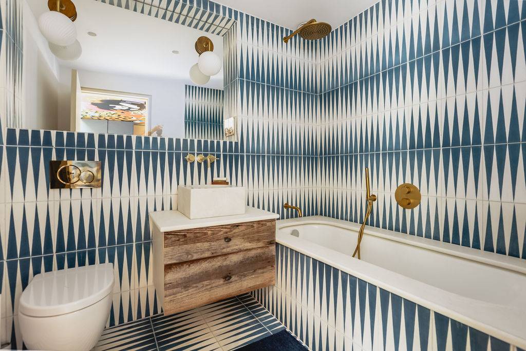 Luxury bathroom with blue and white geometric tile walls, wooden vanity, and freestanding tub, Love Locations GU32.