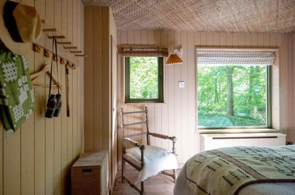 Bright bedroom corner featuring a vintage wooden armchair placed by a window framing dense green trees, perfect for quiet drama scenes, Love Locations.