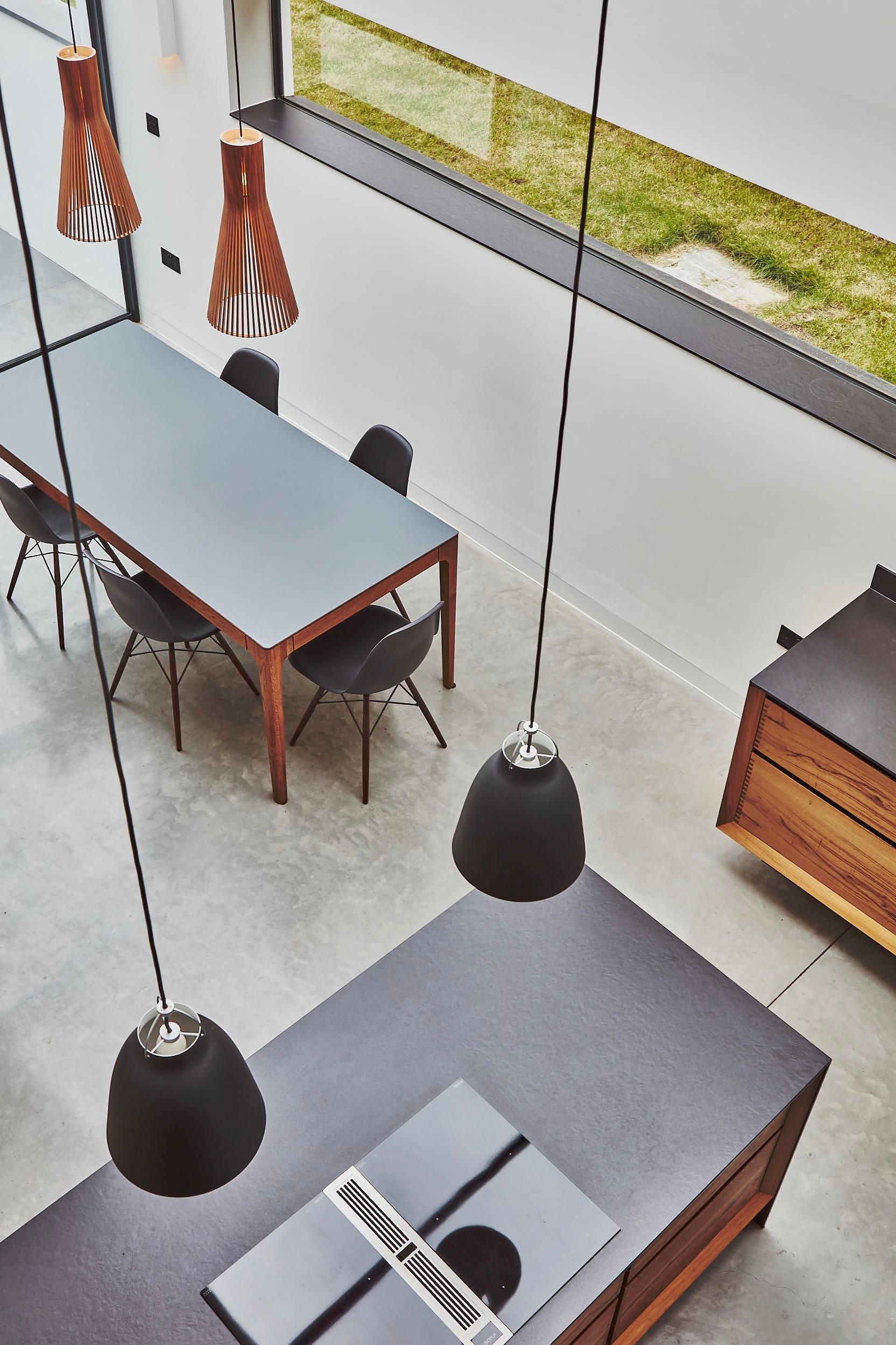 High-angle perspective looking down into a double-height dining room with black pendant lights and concrete floor, Love Locations TW1.