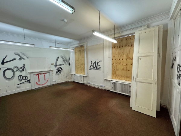 Atmospheric derelict room with extensive black spray paint tags and boarded windows for realistic urban drama filming, Love Locations.