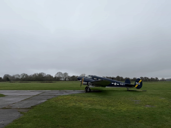 Vintage military-style aircraft parked on a wide grass airfield runway in Northamptonshire, NN17, perfect for period war drama filming, Love Locations.