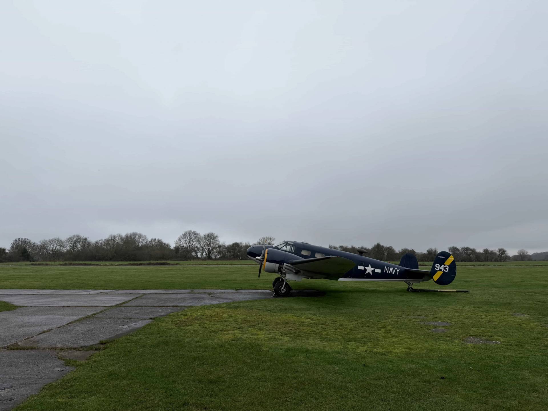 Vintage military-style aircraft parked on a wide grass airfield runway in Northamptonshire, NN17, perfect for period war drama filming, Love Locations.
