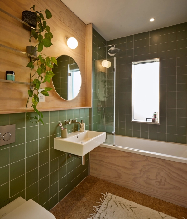Modern bathroom wrapped in forest green square tiles with white basin and integrated bathtub, Love Locations E17.