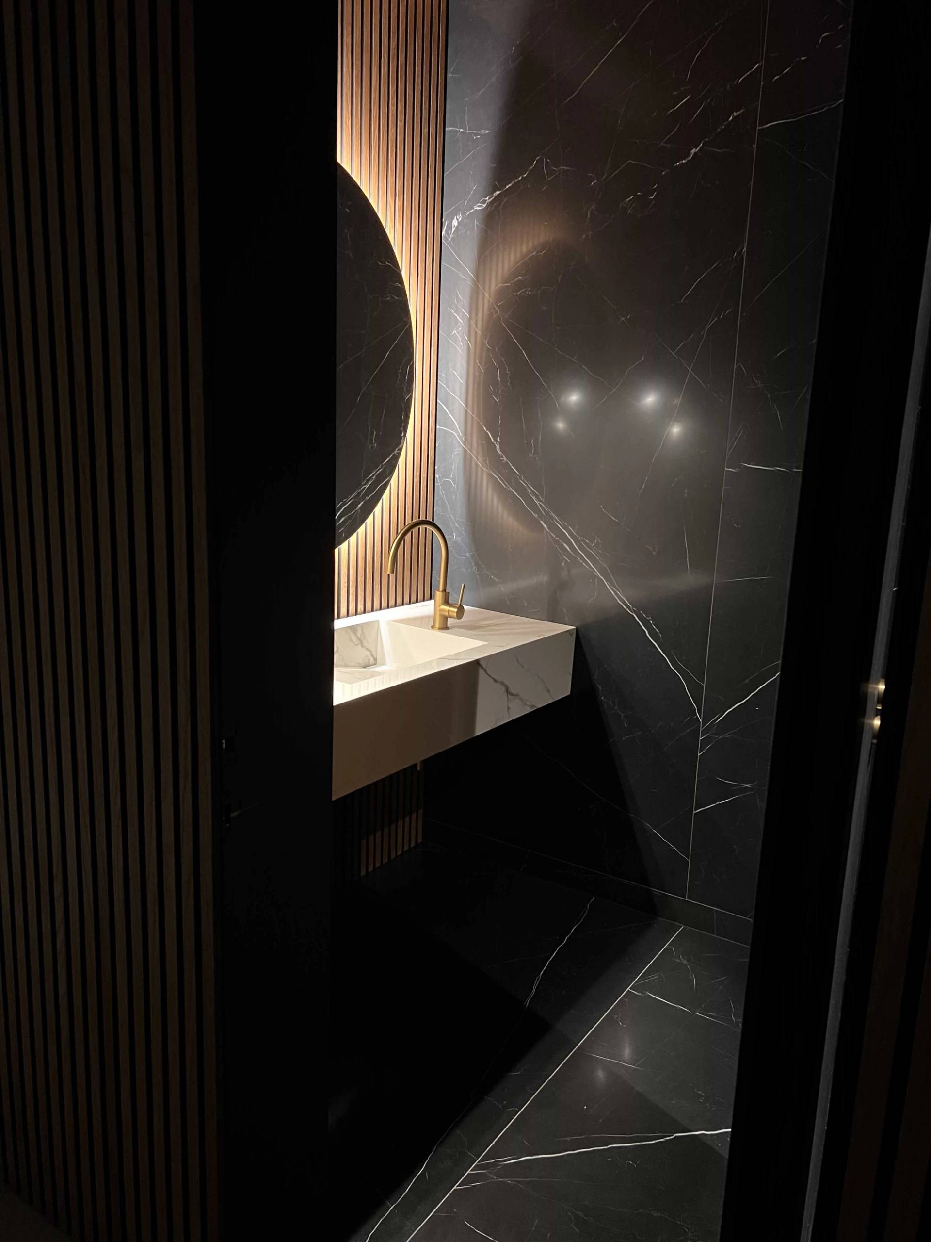 Dark luxury cloakroom toilet featuring a rounded backlit LED mirror, fluted gold splashback, and integrated vanity lighting, ideal for high-end interior features, Love Locations N3.