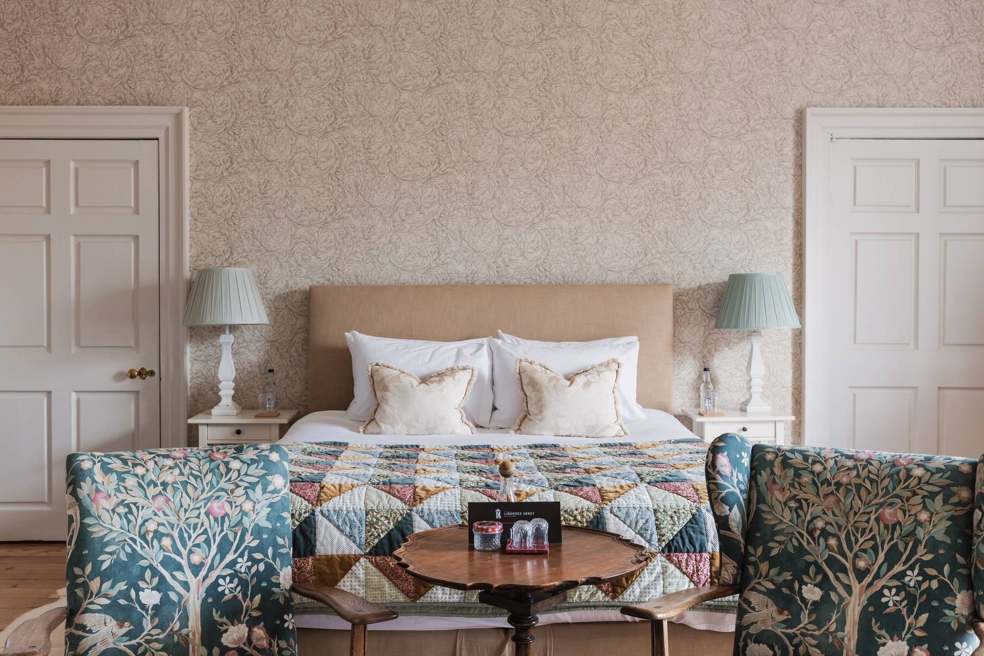 Neutral master bedroom with upholstered bedstead, bedside lamps, and patterned quilt, Love Locations KY15.