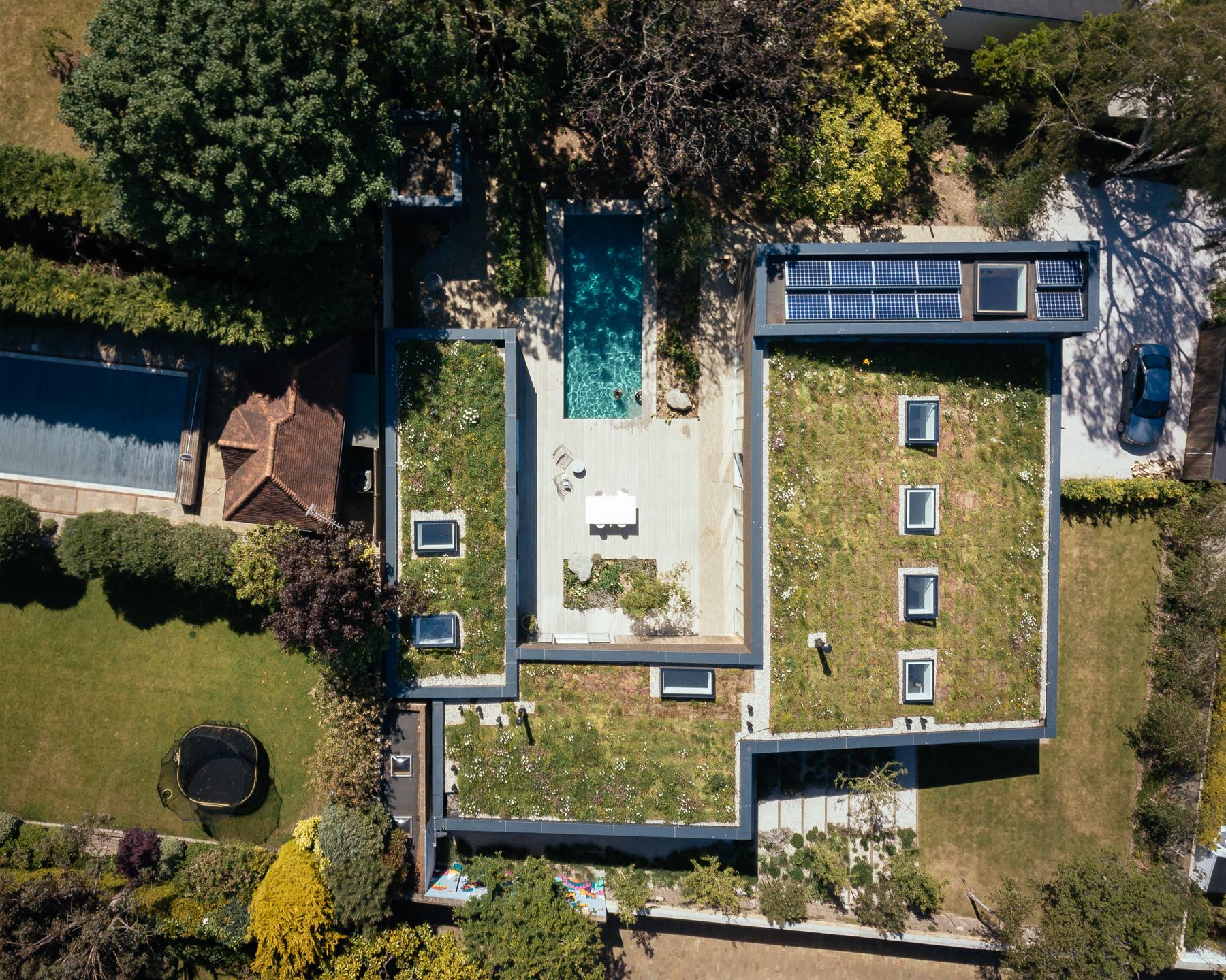 Aerial drone view of a modern green-roofed single-storey architectural home with a private swimming pool, Love Locations BN3.