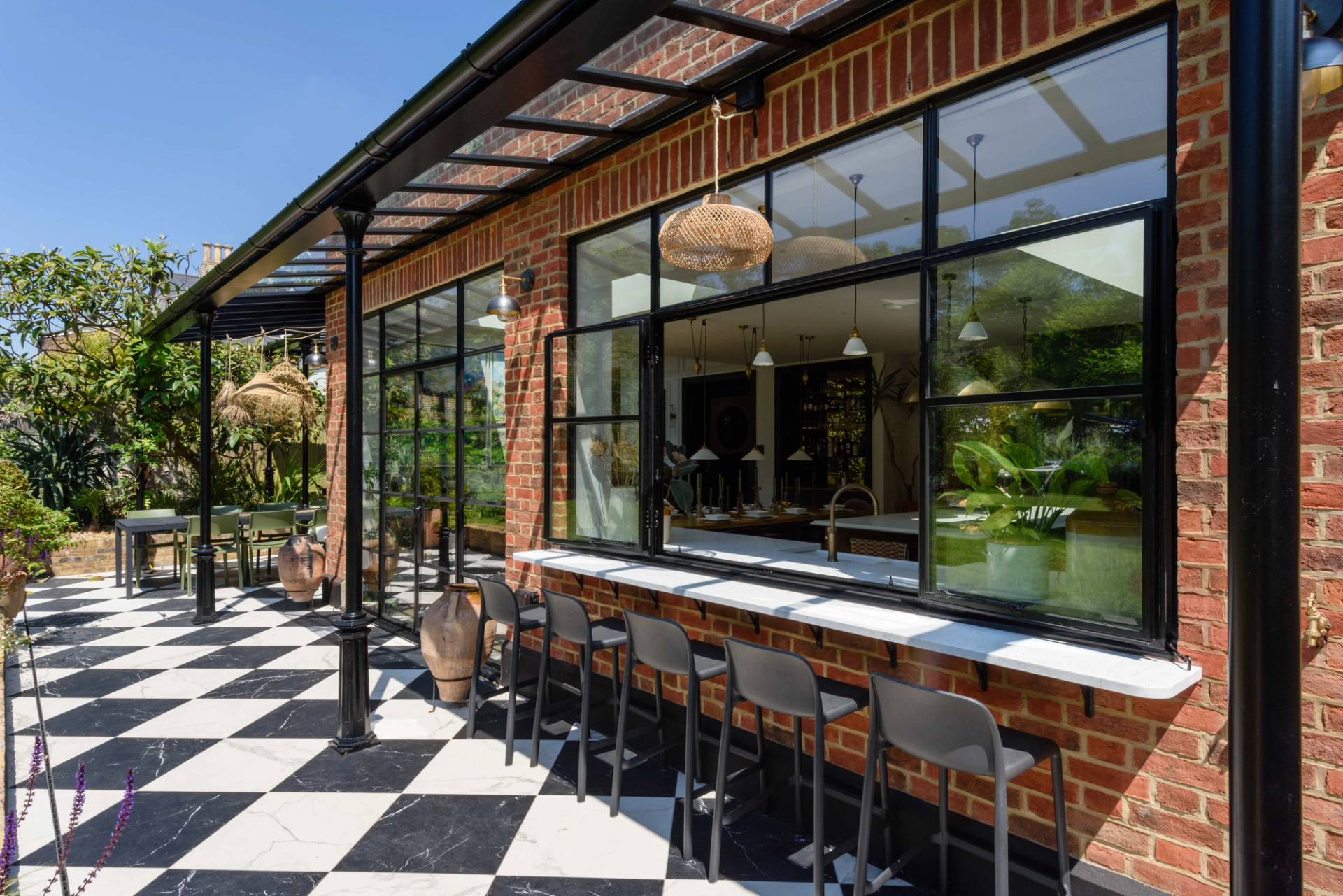 Outdoor bar seating counter set outside large black crittall kitchen windows with checkered patio tiles, Love Locations TW11.