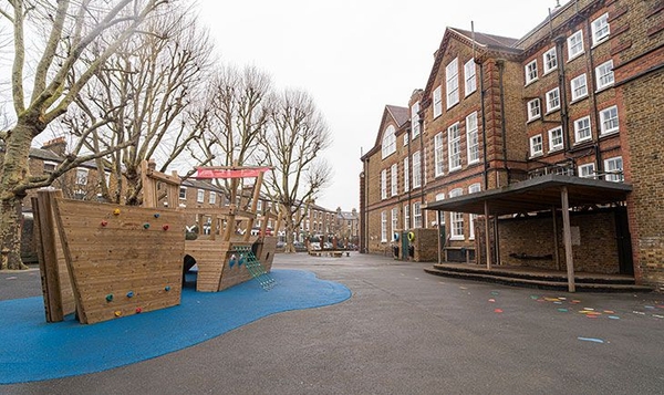Expansive primary school playground yard with a wooden play ship and historic brick school building backdrop, Love Locations N4.