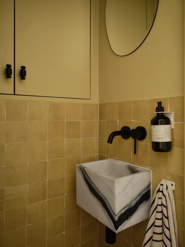 Love Locations block stone bathroom shoot location Lewisham SE23: Guest cloakroom showcasing a monolithic zebra marble sink basin, matte black wall taps, and warm ochre tiling, ideal for beauty ads.