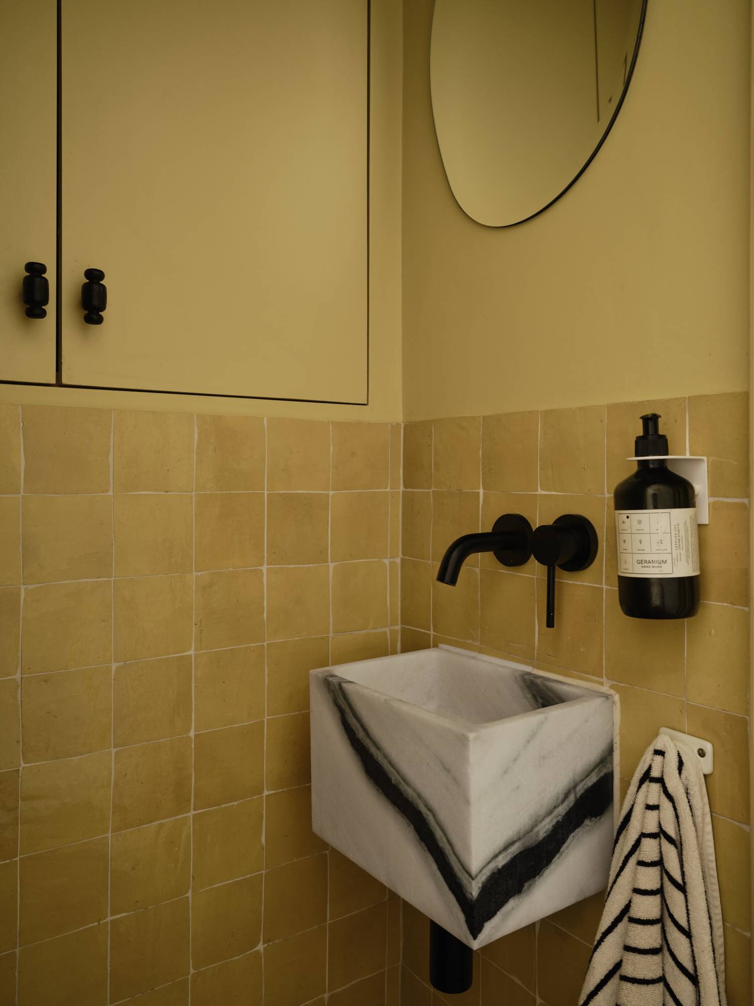 Love Locations block stone bathroom shoot location Lewisham SE23: Guest cloakroom showcasing a monolithic zebra marble sink basin, matte black wall taps, and warm ochre tiling, ideal for beauty ads.