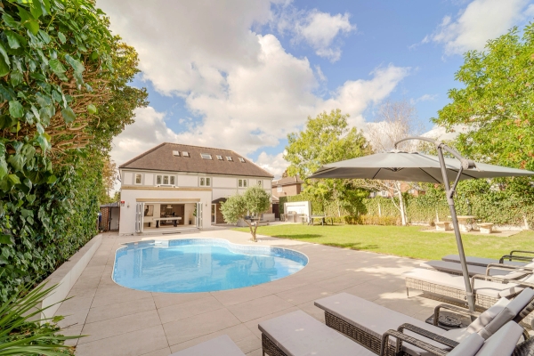 Curved outdoor pool on a paved patio terrace set behind a luxury detached house facade, Love Locations RM11.
