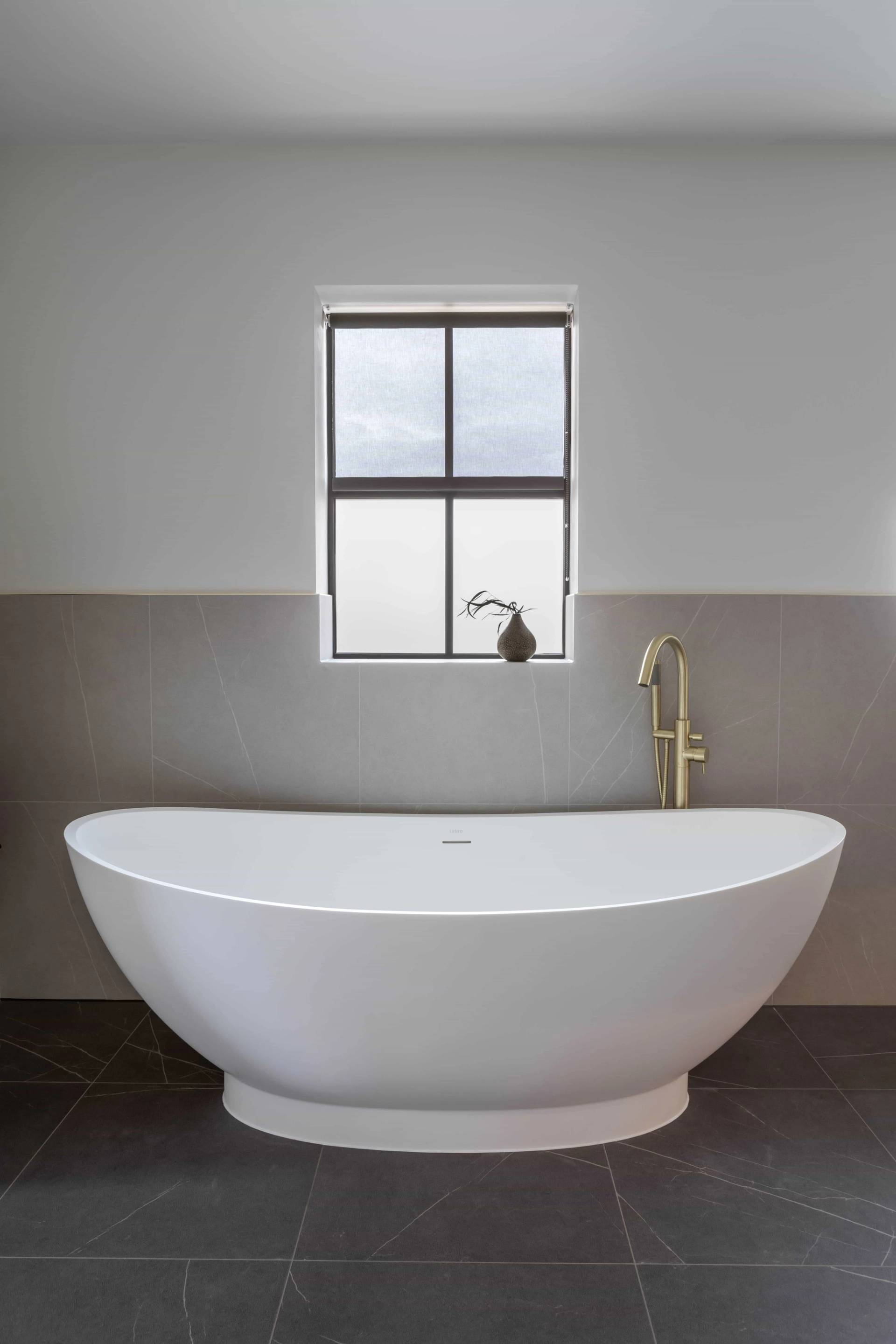 Freestanding white soaking bathtub set against a grey and blush painted feature wall under a sash window, Love Locations HP18.