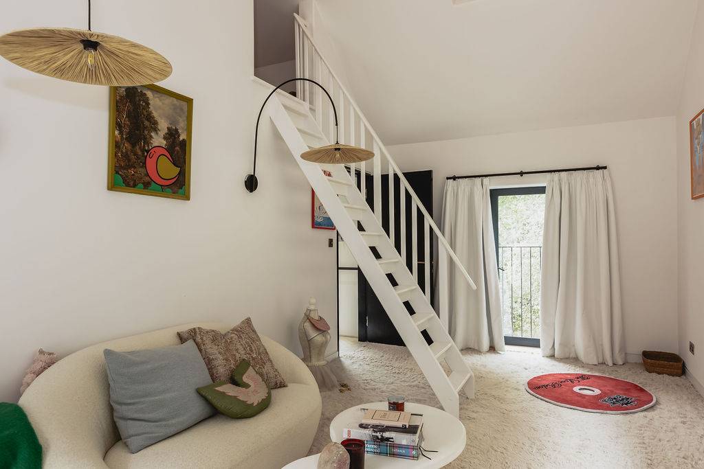 Loft bedroom setup with a mezzanine ladder, sofa seating, and bright white painted walls, Love Locations GU32.