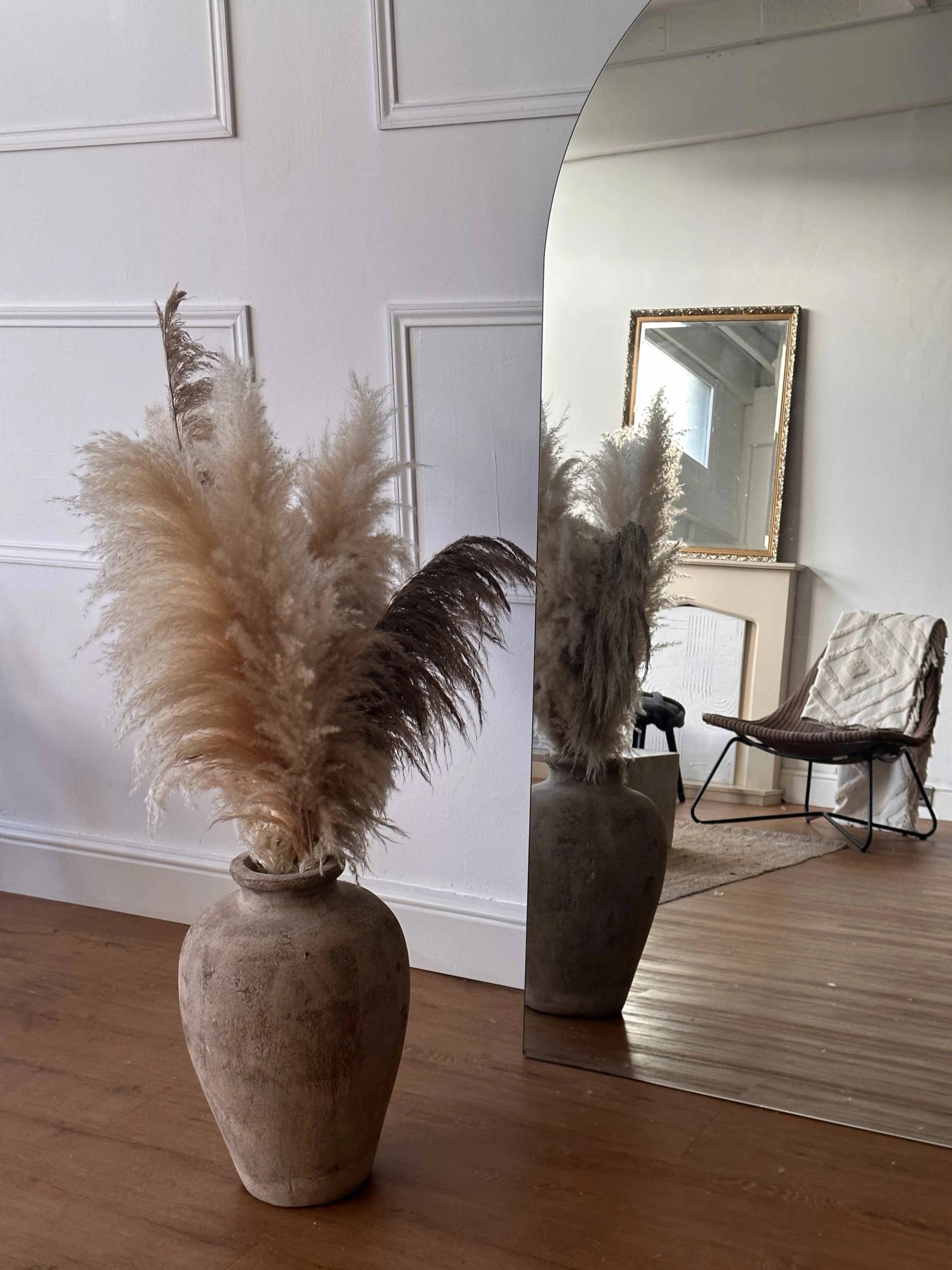 Rustic ceramic vase with dried pampas grass standing beside a tall arched floor mirror reflecting a fireplace backdrop, perfect for homeware brand marketing, Love Locations SW8.
