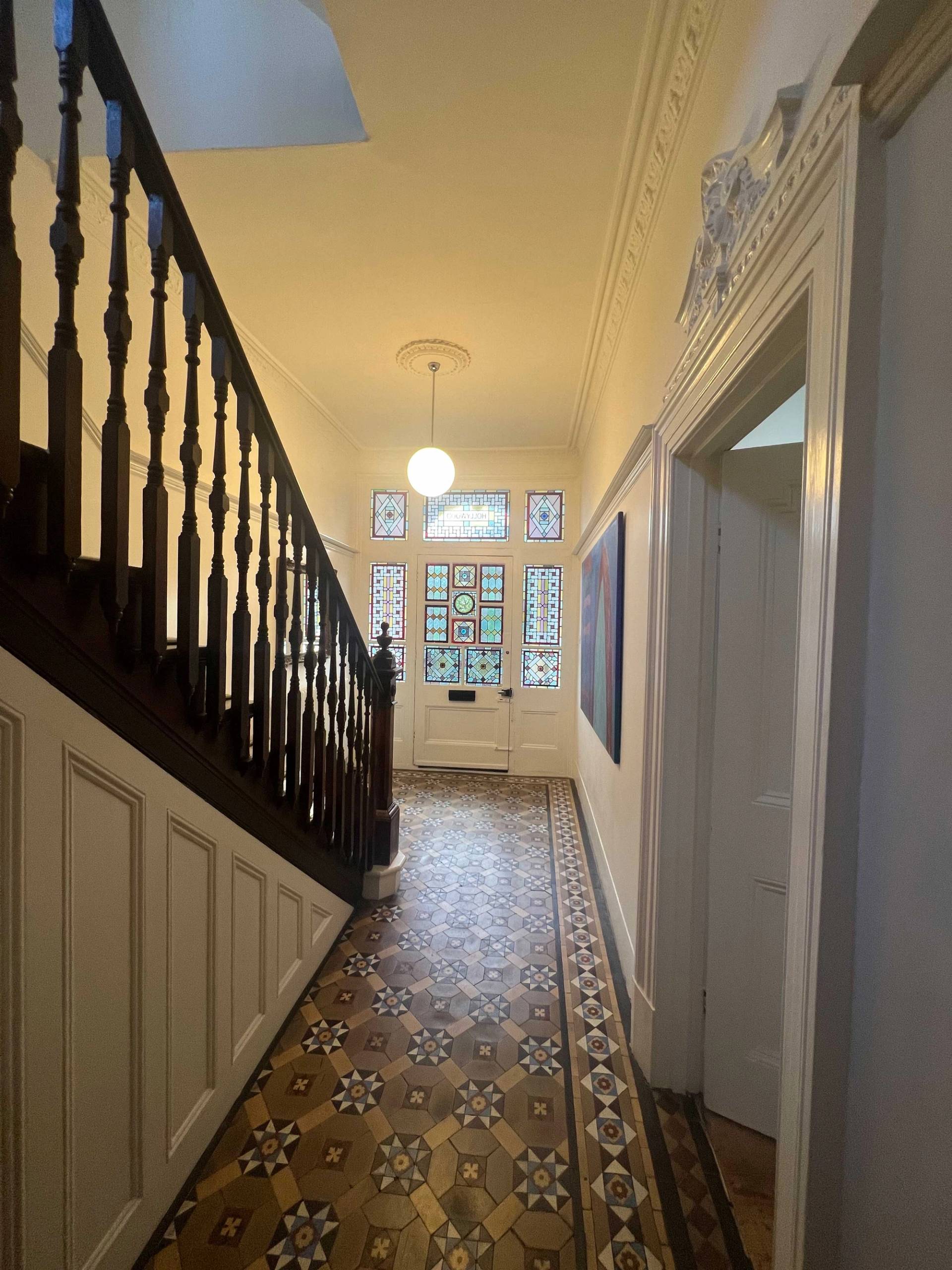 Victorian hallway passage featuring dark wood banisters, tessellated floor tiles, and stained glass front door transom, Love Locations Denmark Hill.