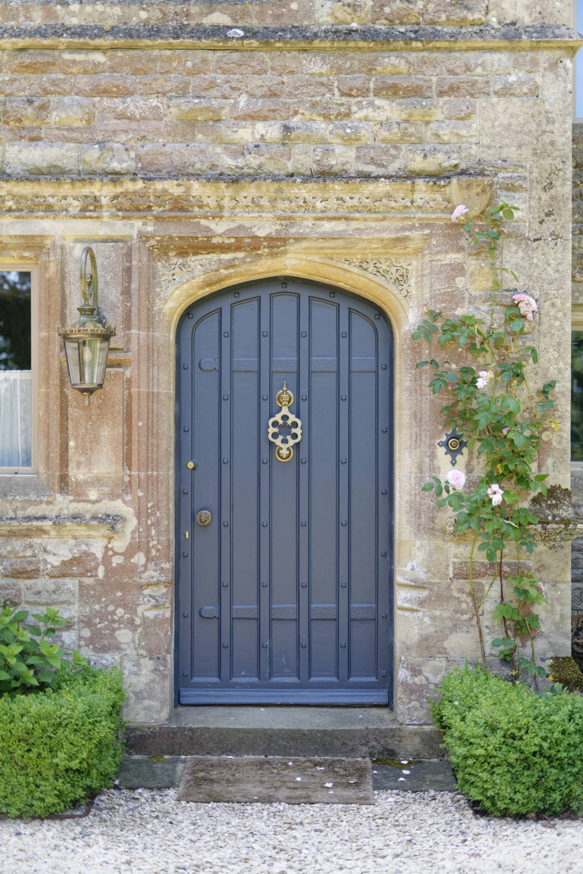 Cotswold stone manor and barn conversion hero cover image in Oxfordshire, OX7 featuring historic stone facade, arched blue front door, outdoor swimming pool, modern black pool house with sauna, veined marble kitchen island, and tennis court estate grounds, the ultimate high-visibility backdrop for feature film productions, TV drama filming, commercial brand campaigns, and luxury editorial photography via Love Locations.