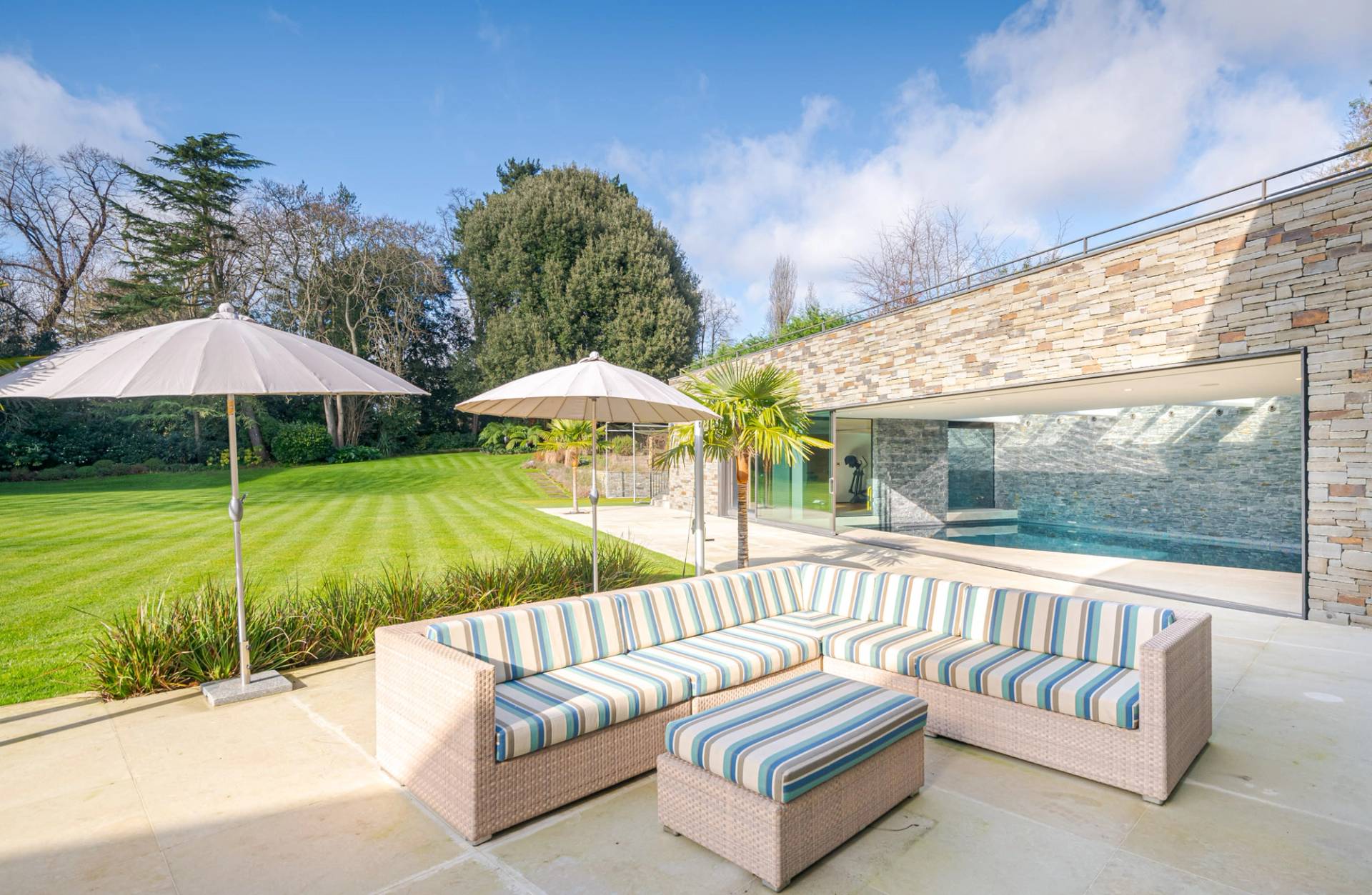 Outdoor lounge terrace featuring striped outdoor sofas, sun umbrellas, and manicured green lawns, ideal for summer campaign filming, Love Locations KT2.