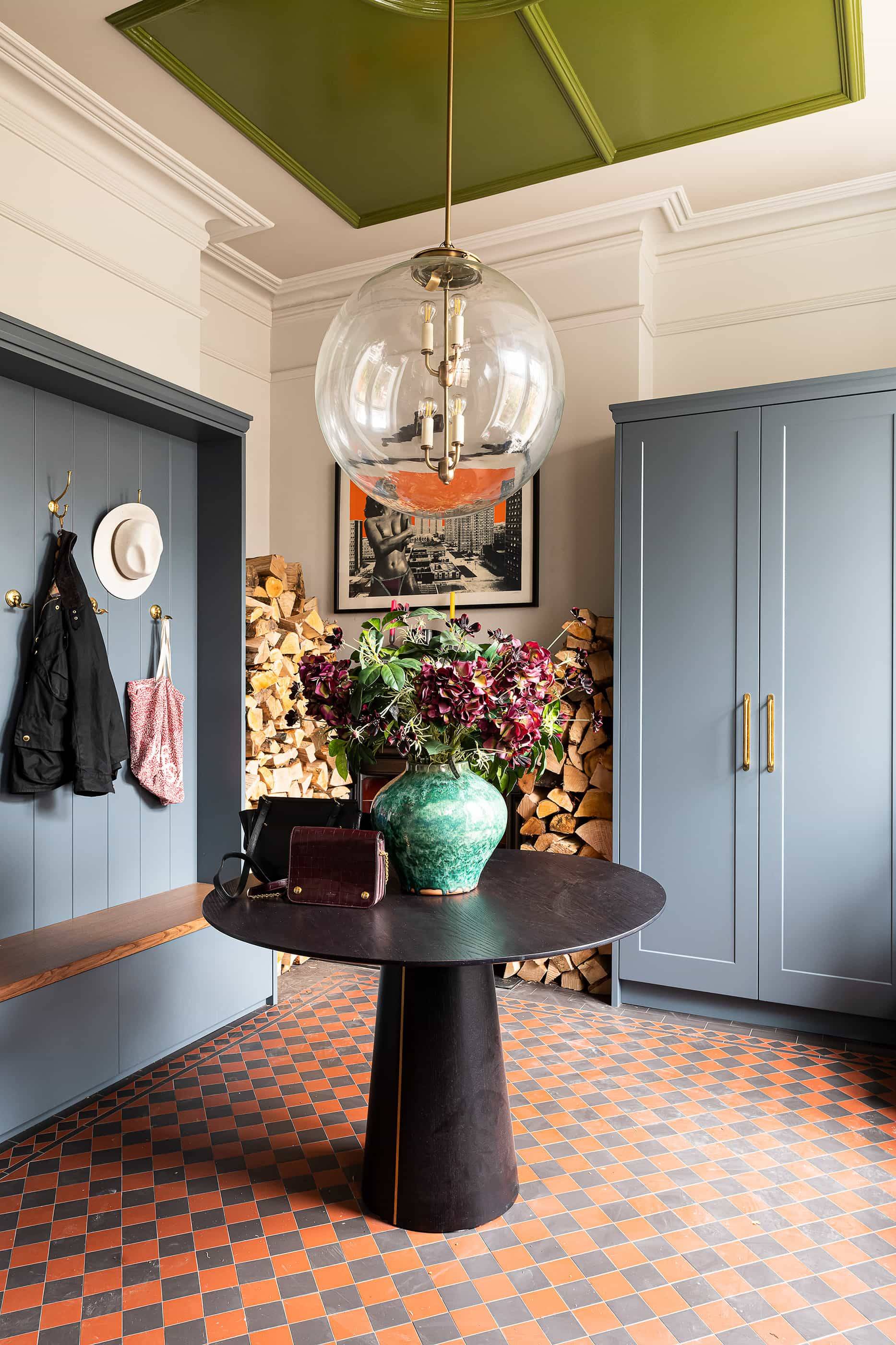Utility boot room entrance featuring blue cabinetry, coat hooks, round dining table, and geometric floor tiles, ideal for country lifestyle brand lookbooks, Love Locations NW6.
