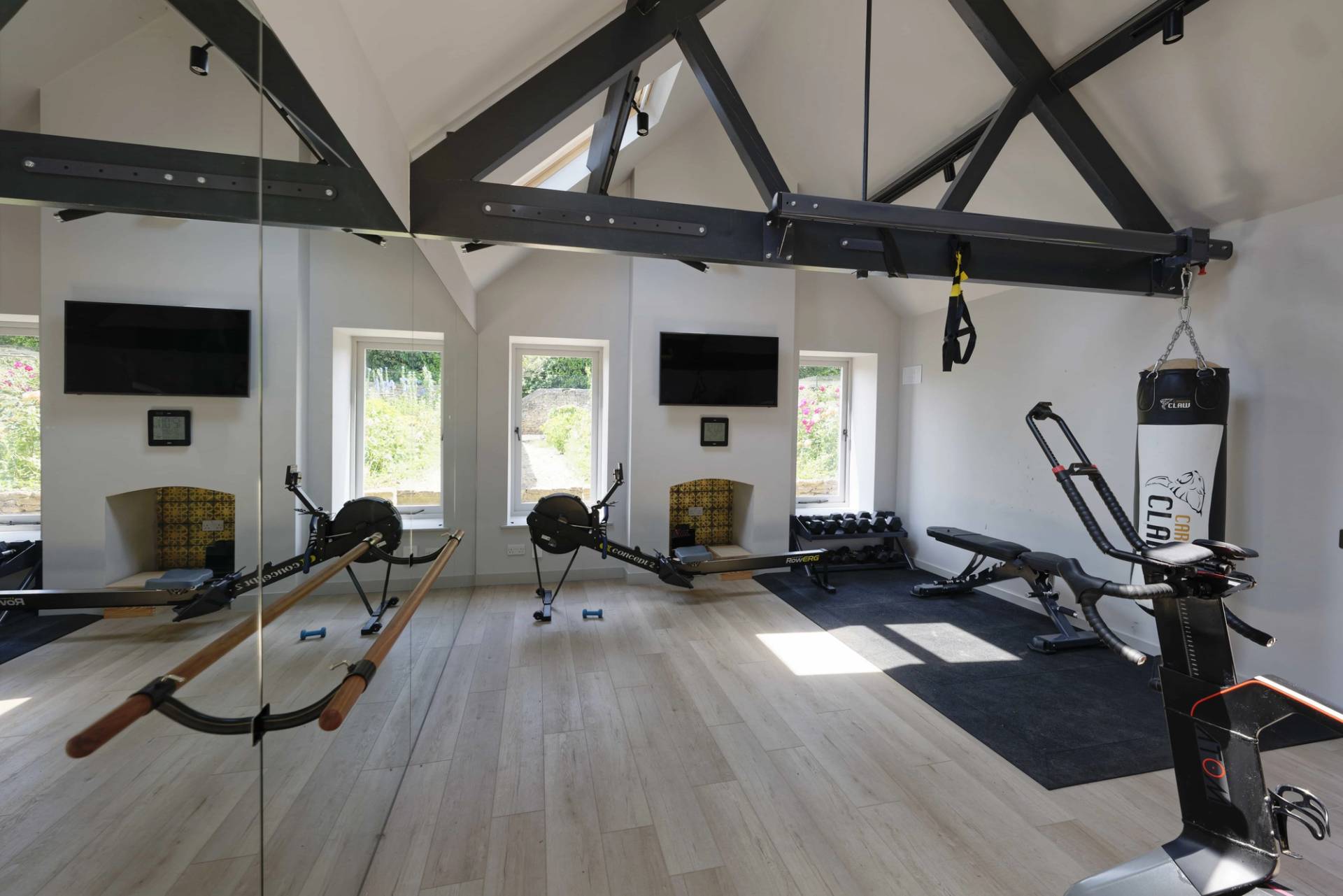 Private home gym setup set under exposed black roof trusses with rowing machines and weights, Love Locations OX7.