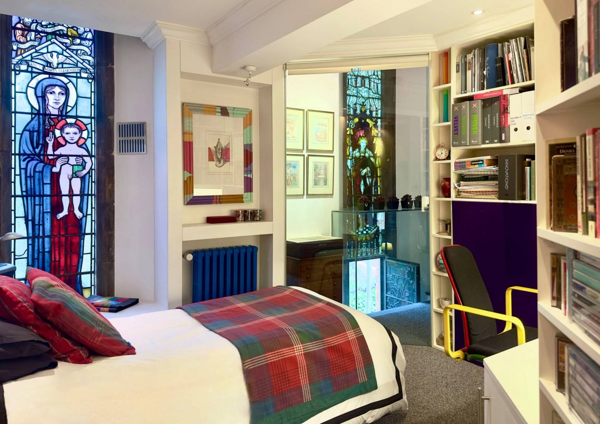 Creative bedroom setup featuring tartan bedding, stained glass windows, and surrounding bookshelves in Oval SE5 by Love Locations.