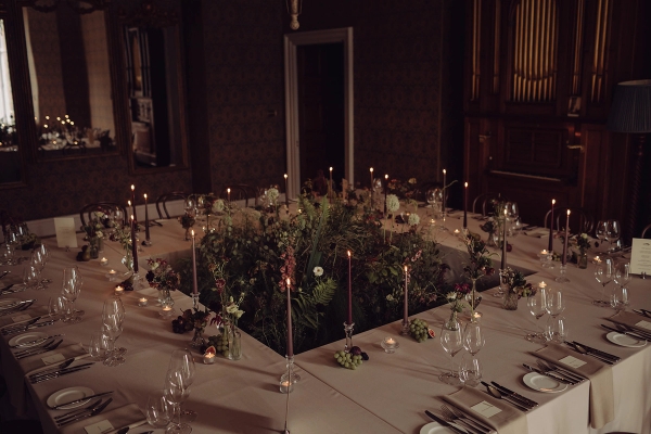 Atmospheric candlelit dining layout around a square central floral display in a dark castle hall, Love Locations KY15.