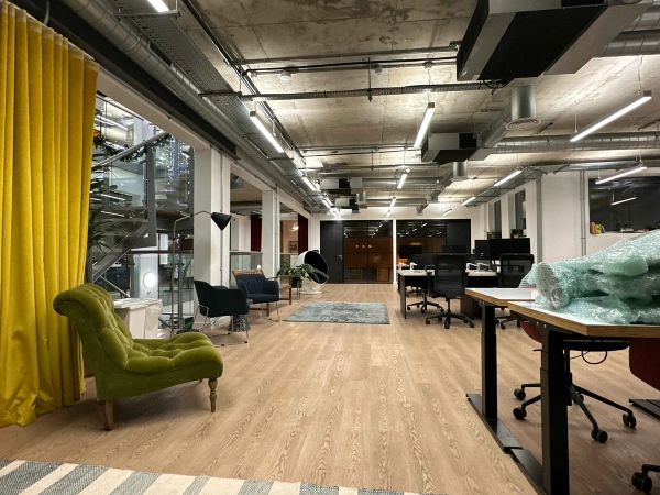 Bright open office space with industrial-style exposed ceiling, floor-to-ceiling yellow curtain, and a green velvet modern chair.