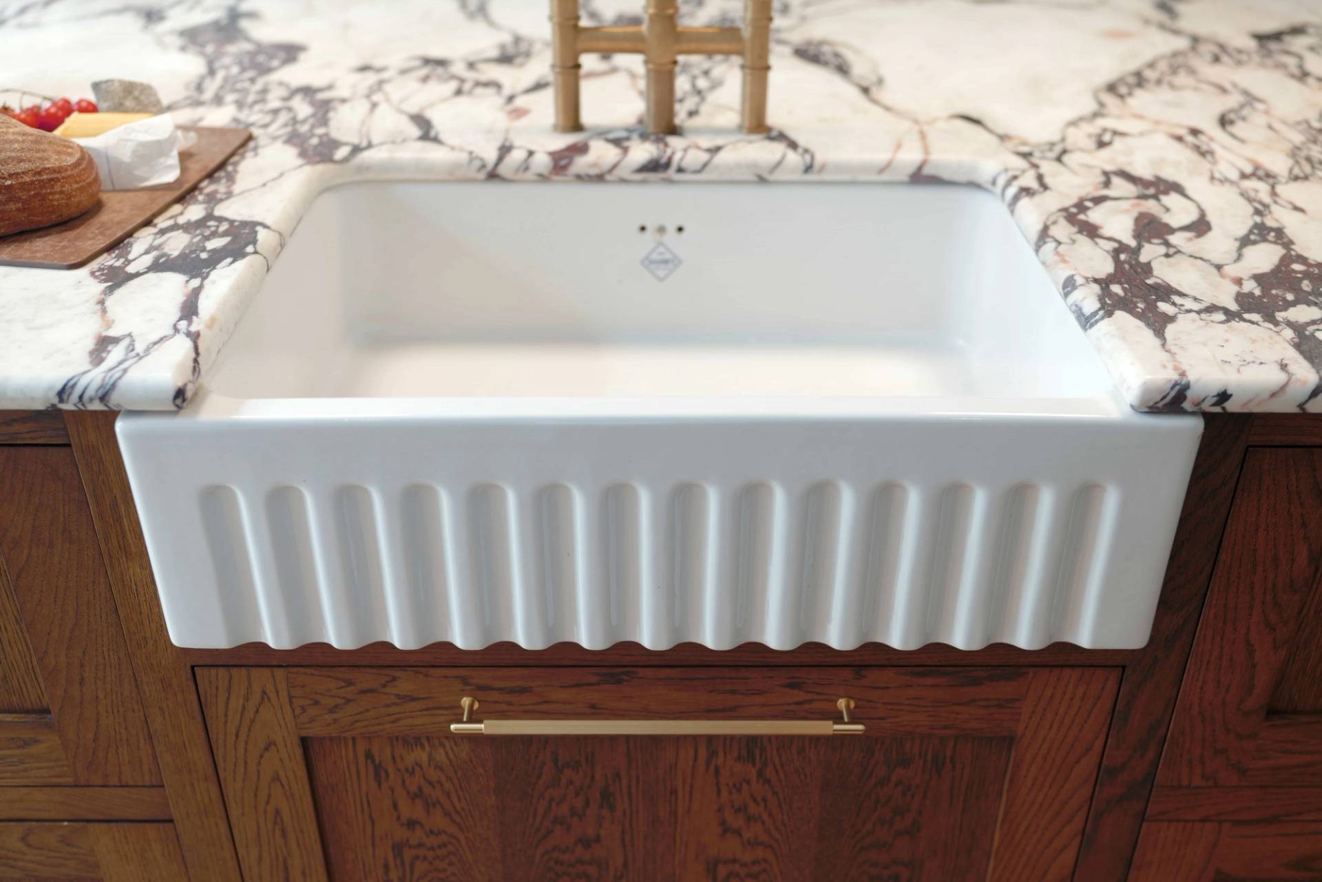 Fluted ceramic sink set on a wooden vanity unit with veined marble splashback, Love Locations OX7.