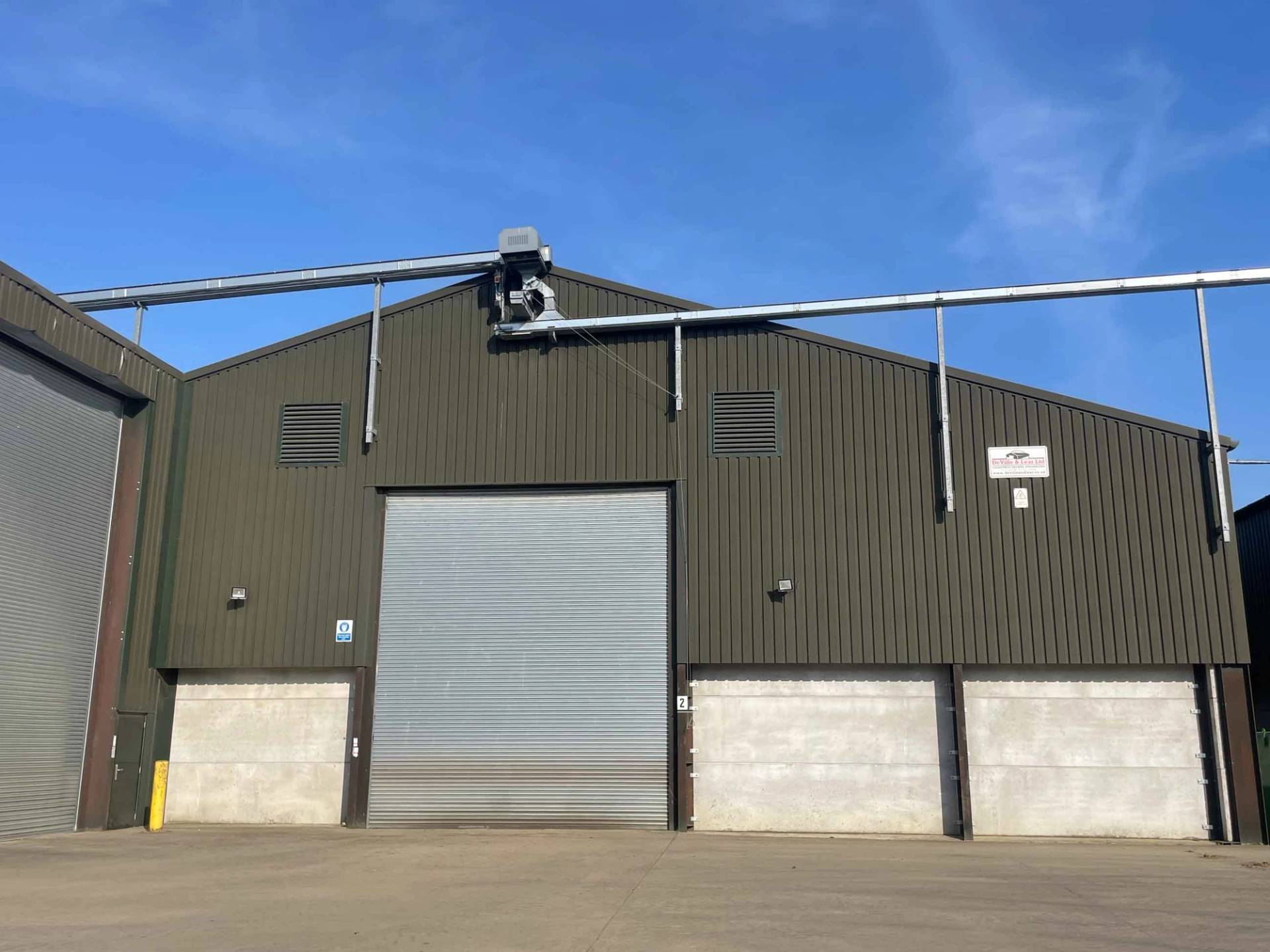 Modern green agricultural storage shed featuring roller shutter doors and concrete foundations in Corby, NN17, Love Locations.