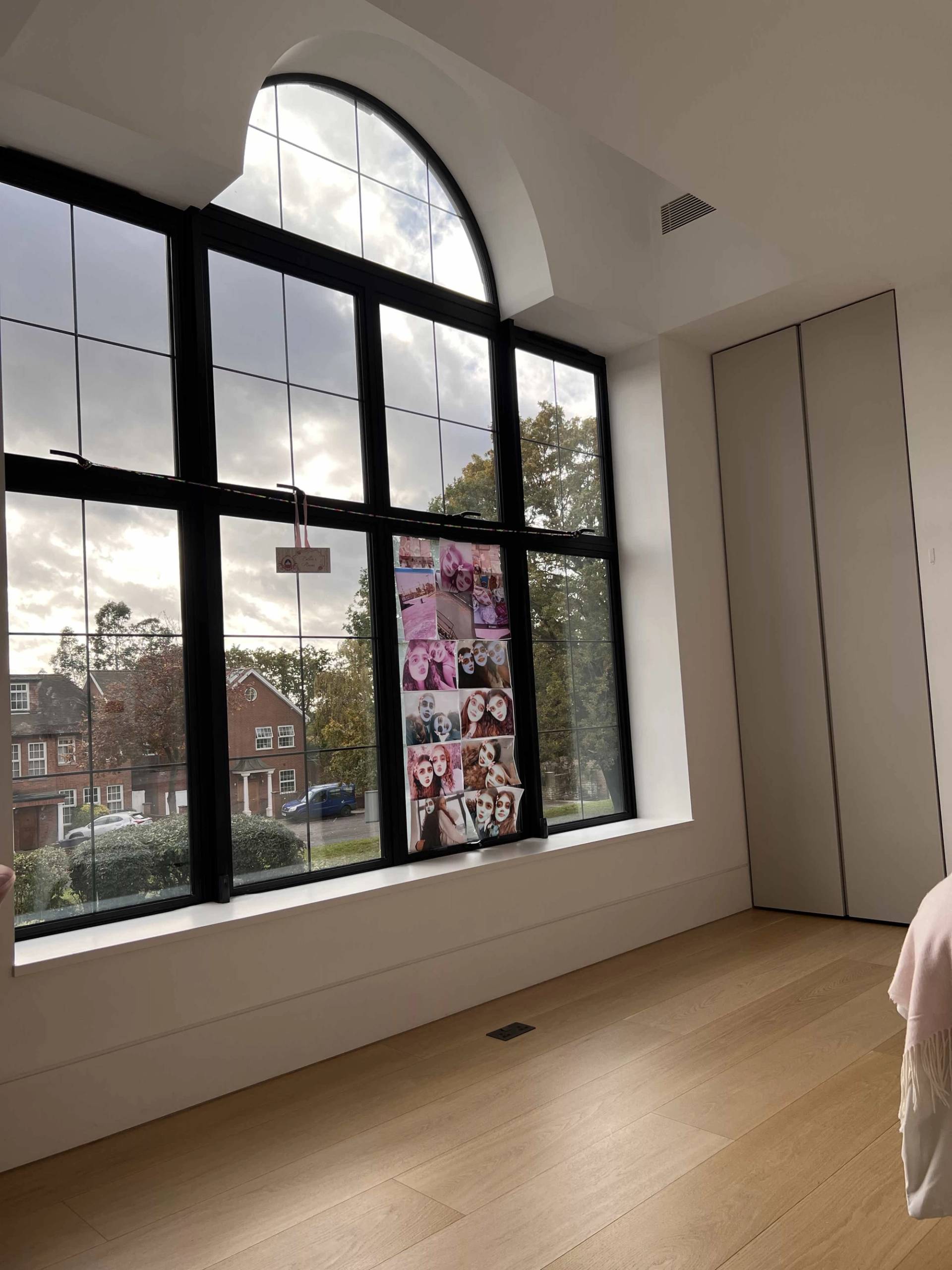 Spacious bedroom featuring large arched black-framed windows, light wood floors, and minimalist wall panelling, perfect for fashion editorial shoots, Love Locations N3.