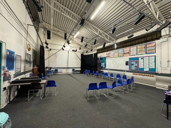Love Locations secondary school drama studio Cockfosters: Large rehearsal space with an industrial ceiling grid and studio stage lighting tracks, optimized for music videos and actor interview setups.