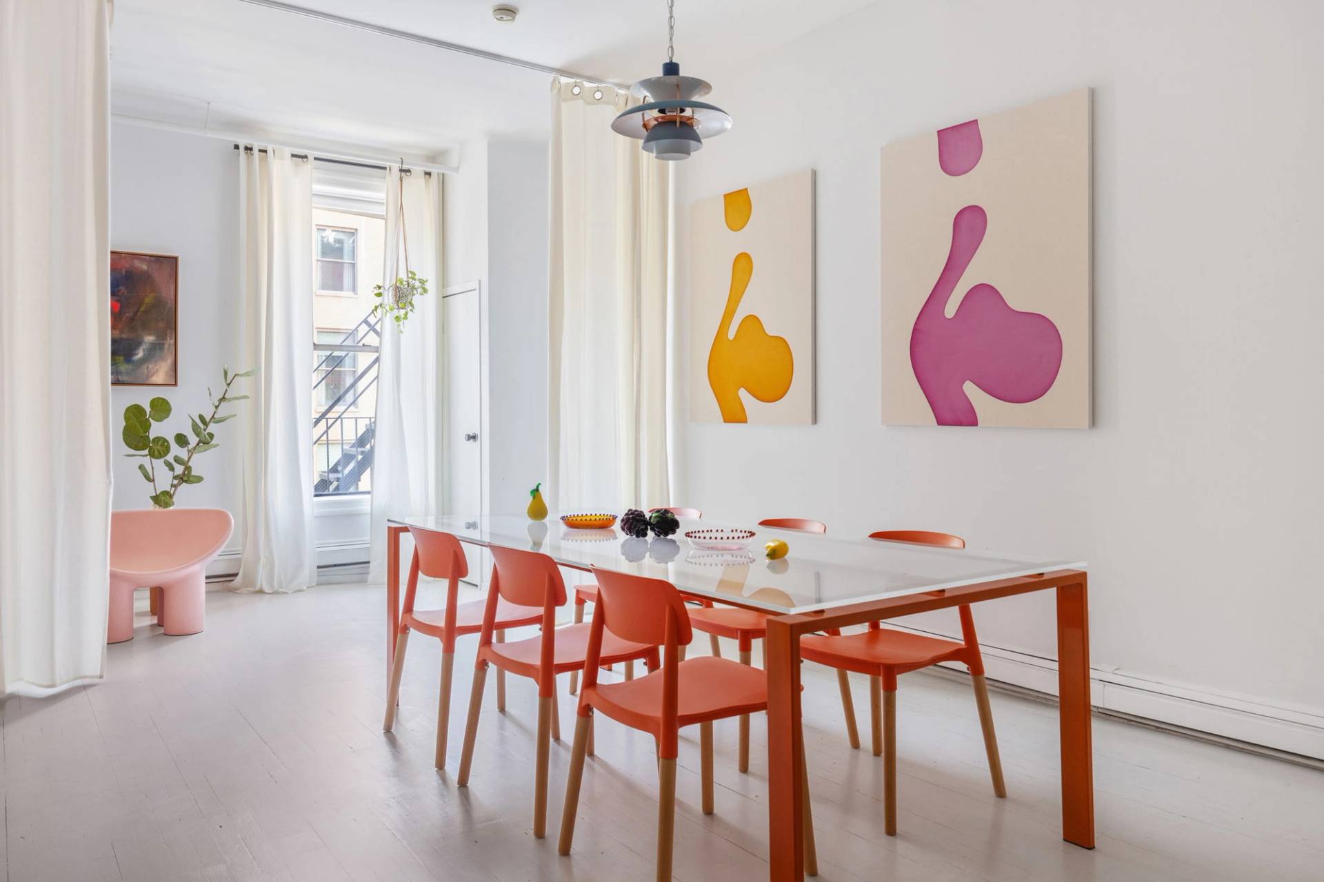 Sunlit dining room film location in a Tribeca artist loft from Love Locations, featuring an orange dining table set, ceiling fan, large windows, and graphic art pieces.