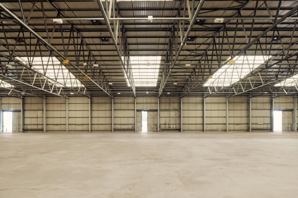 Large-scale empty industrial warehouse film studio with concrete flooring and overhead skylights, ideal for vehicle commercials, available through Love Locations.