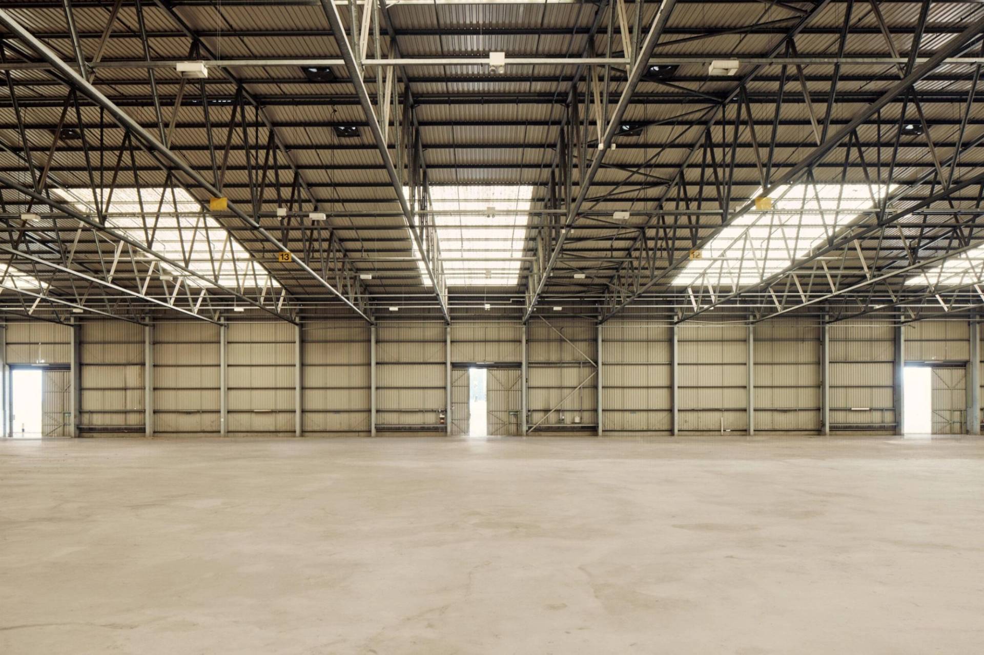 Large-scale empty industrial warehouse film studio with concrete flooring and overhead skylights, ideal for vehicle commercials, available through Love Locations.