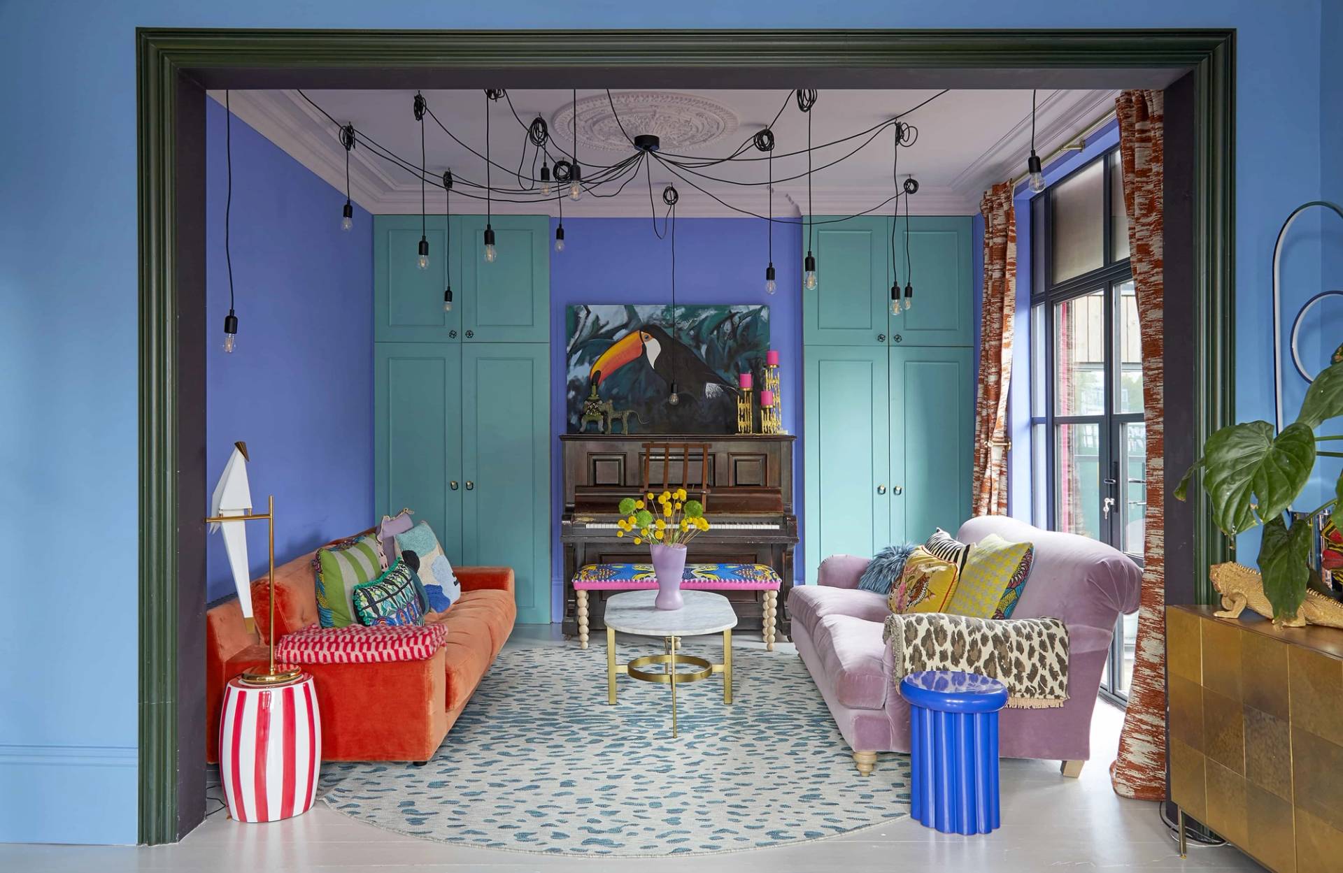 Maximalist sitting room featuring purple built-in wardrobes, pink sofa, orange armchair, and blue ceiling, Love Locations SE6.
