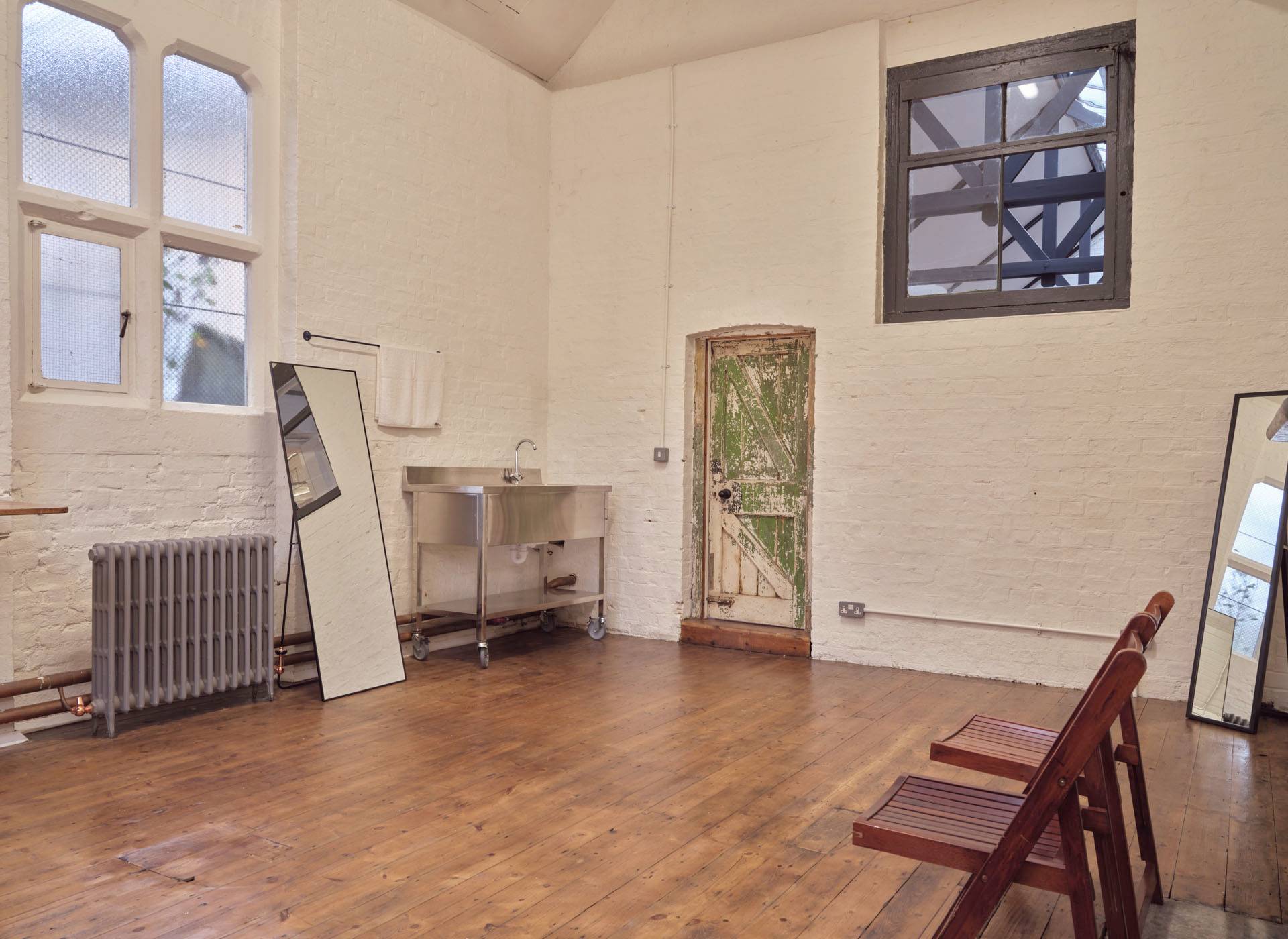 Green room or production office space featuring a stainless steel sink, large mirror, and wooden seating, Love Locations E2.