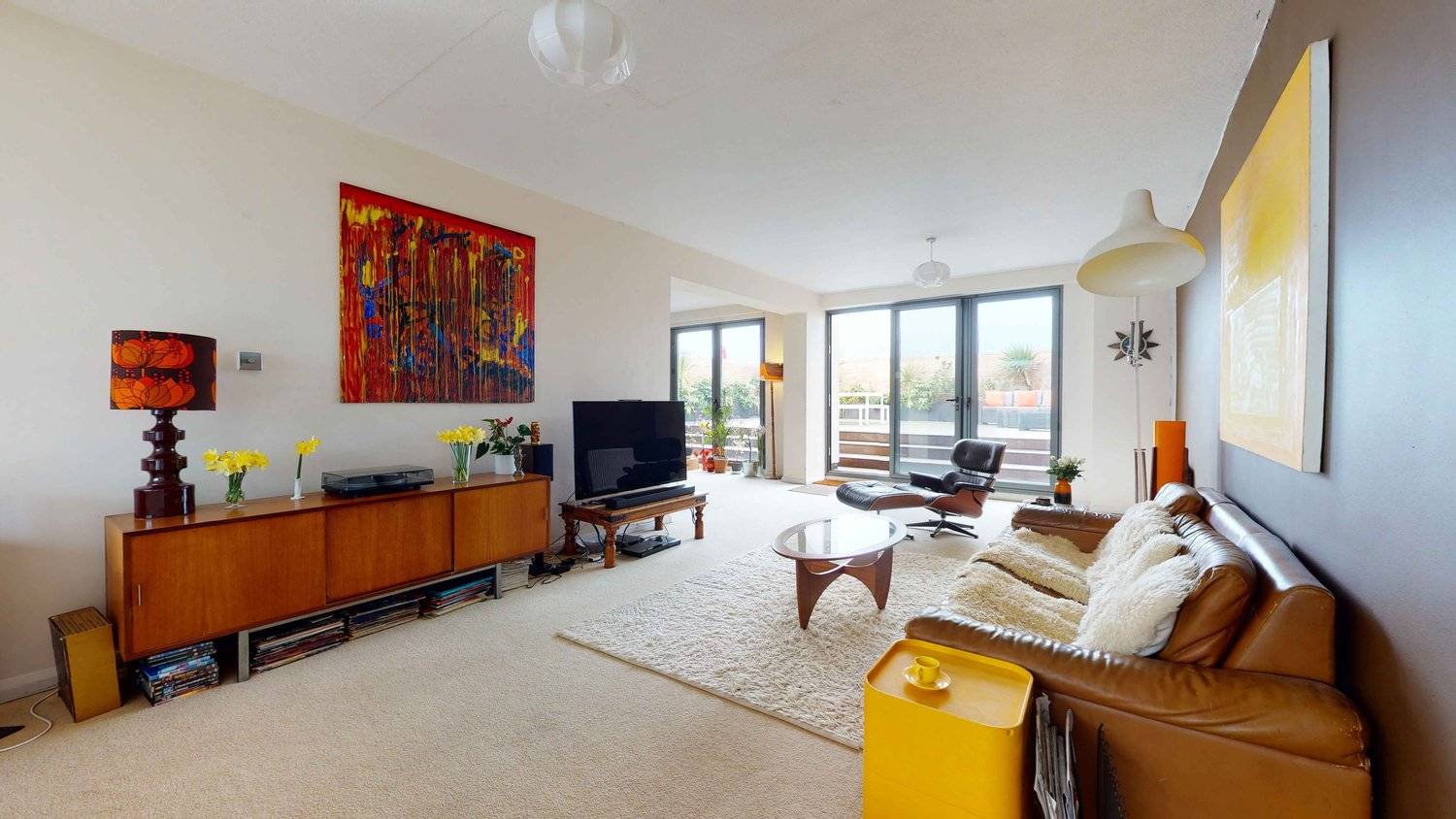 Bright 1970s open-plan living room with brown accent wall, yellow artwork, tan leather sofa, and arc floor lamp, Love Locations SW16.