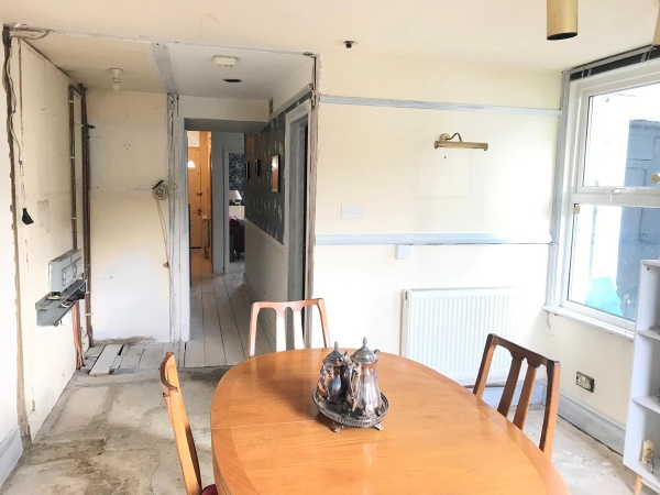 Rustic dining area showing a large wooden oval table and chairs set against partially stripped plaster walls, perfect for gritty lifestyle photography, Love Locations SE25.